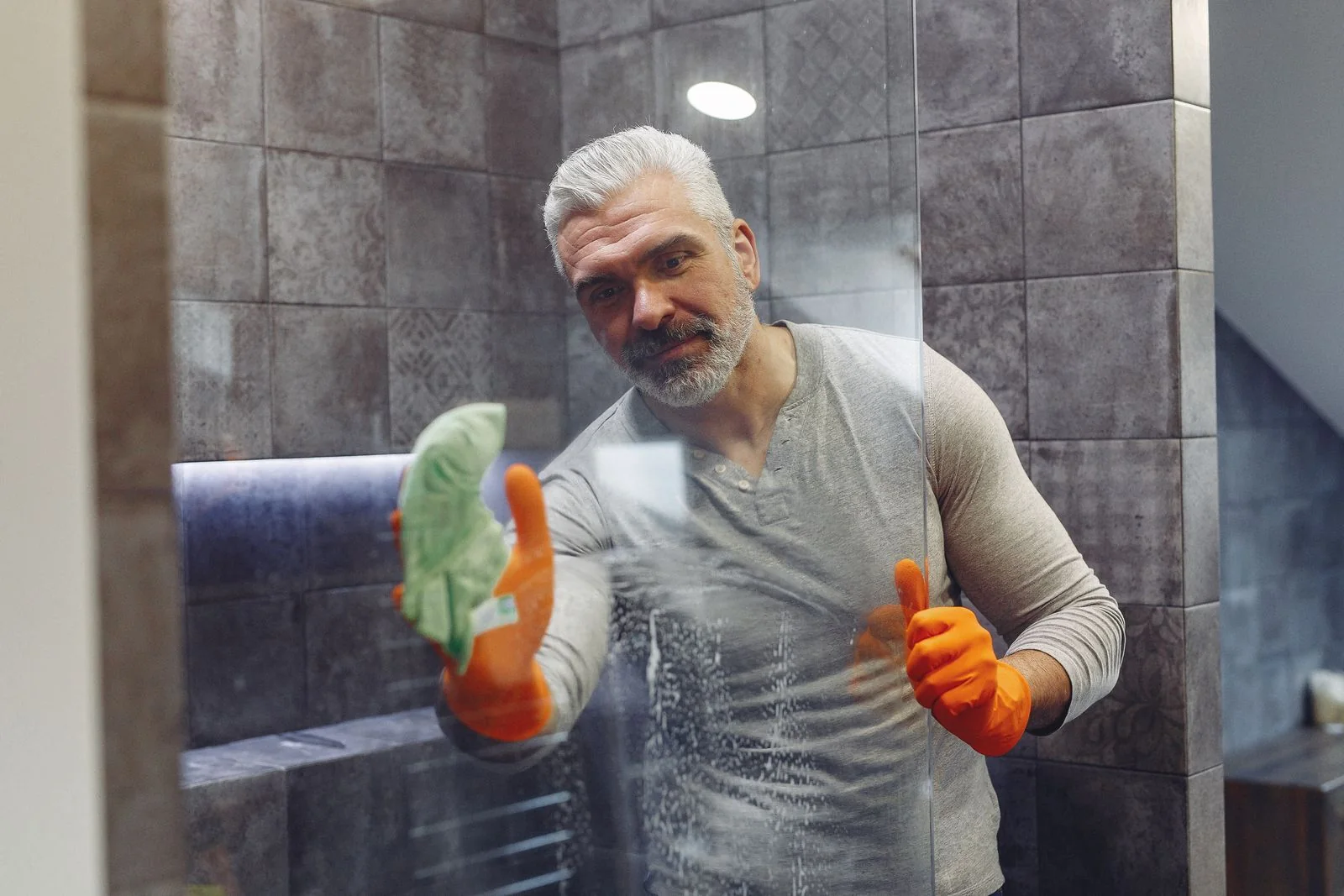 Man cleaning shower glass in a tiled bathroom.